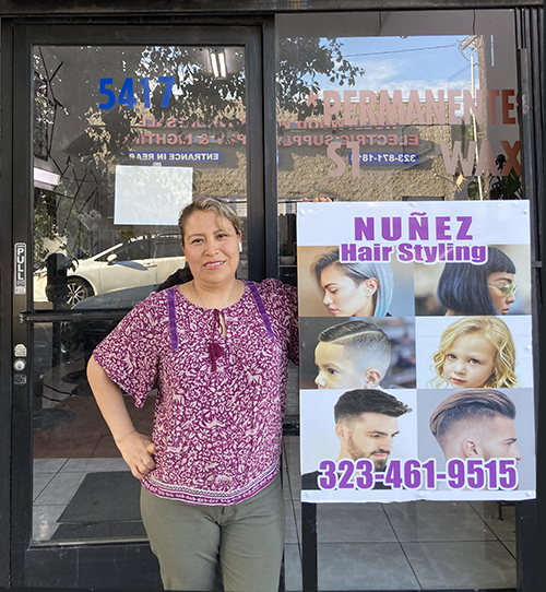 Concepcion Nuñez, owner of Nuñez Hair Styling in Hollywood, wearing a pink peasant blouse and smiling while standing ouside her business