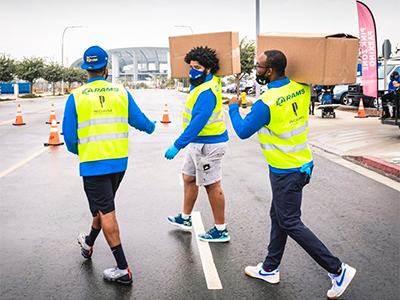 Crenshaw YouthSource Center participant Joseph Merchain (center) carries items in a parking lot at SoFi Stadium, the home base for the Los Angeles Rams
