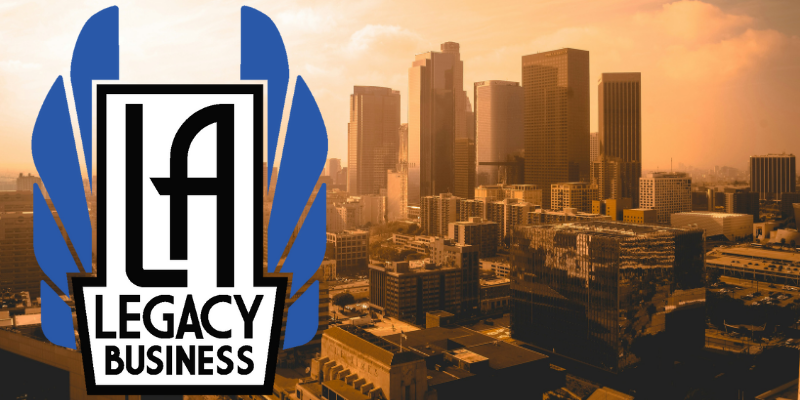 L.A. Legacy Business logo (program name in a white art deco font flanked by art deco style blue wings) over an image of downtown Los Angeles at golden hour sunset